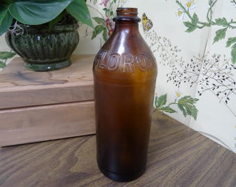 May include: A vintage amber glass bottle with a narrow neck and a threaded top. The word CLOROX is embossed in capital letters around the shoulder of the bottle. The glass is translucent brown, showing a smooth, cylindrical body and a rounded base.