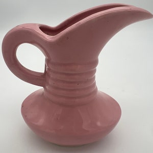 May include: A pink ceramic pitcher with a wide spout and a rounded base. The pitcher has a textured design around the middle.