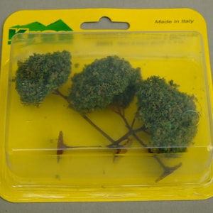 Könnte beinhalten: Eine Packung mit drei kleinen grünen Modellbäumen, verpackt in einem durchsichtigen Plastikbehälter mit gelbem Hintergrund. Die Verpackung trägt den Hinweis "Made in Italy".