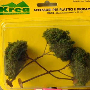 Könnte beinhalten: Eine Packung mit vier grünen Modellbäumen, jeder mit einem braunen Stamm und Ästen. Die Verpackung ist gelb und hat den Text "Krea Modellismo" und "Accessori per Plastici e Diorami 2002 Alberi di bosco medi h. 12 cm." aufgedruckt. Hergestellt in Italien.