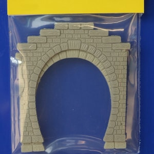 May include: A grey plastic model of a brick tunnel archway. The archway is designed for use in model railway or dioramas.