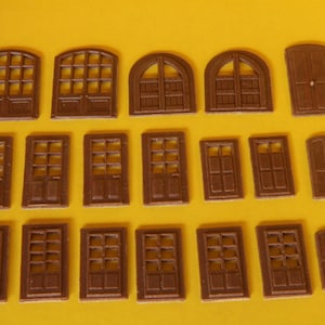 May include: A collection of 18 miniature wooden doors and windows, all in a brown color. The doors and windows are various styles, including arched, rectangular, and with different pane patterns.