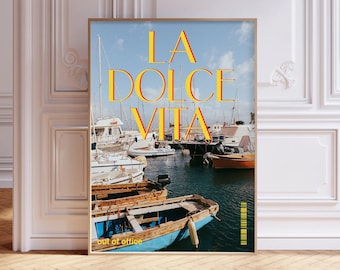 May include: A poster with a blue and white photo of boats in a harbor. The text "LA DOLCE VITA" is in yellow letters with red outlines. The text "out of office" is in smaller letters at the bottom of the poster.