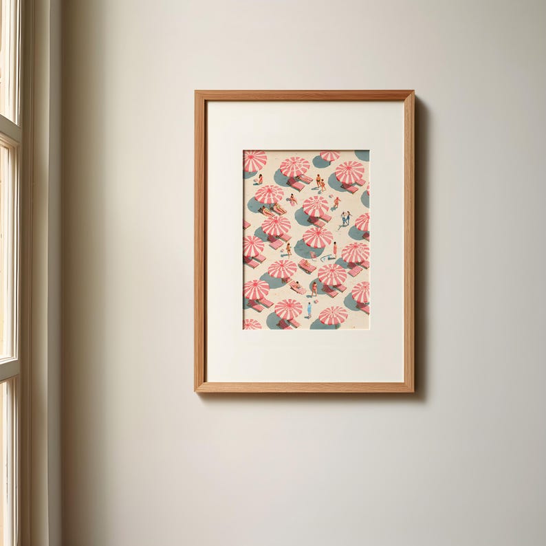May include: Framed art print featuring a beach scene with pink and white striped umbrellas, beach towels, and small figures of people. The artwork is set against a light beige background, with shadows suggesting sunlight. The frame is made of light brown wood.