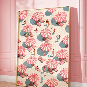 May include: A framed art print depicts a beach scene with numerous red and white striped umbrellas, beach chairs, and people. The artwork has a vintage aesthetic, with a light beige background and a gold frame. The scene is set against a pink wall and wooden floor.