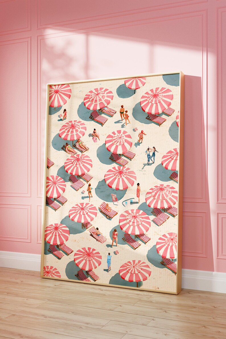 May include: A framed art print depicts a beach scene with numerous red and white striped umbrellas, beach chairs, and people. The artwork has a vintage aesthetic, with a light beige background and a gold frame. The scene is set against a pink wall and wooden floor.
