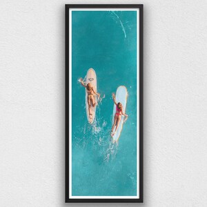 May include: Two people on surfboards in a turquoise ocean. The surfboards are white and yellow. The people are wearing swimsuits and are lying on their stomachs.