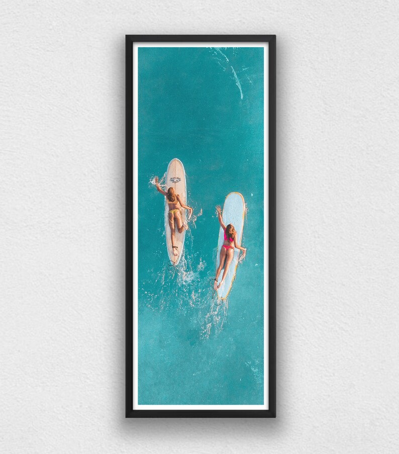 May include: Two people on surfboards in a turquoise ocean. The surfboards are white and yellow. The people are wearing swimsuits and are lying on their stomachs.