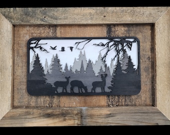 May include: A black wooden wall art piece with a silhouette of a forest scene with deer and birds. The art is framed in a rustic wood frame.