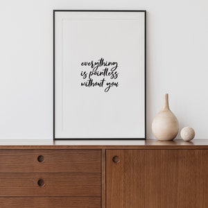 May include: Black and white framed print with the text "everything is pointless without you" hanging on a white wall above a brown wooden dresser with two drawers.