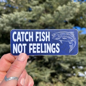 Könnte beinhalten: Ein blauer und weißer Aufkleber mit einem Fisch und dem Text "Catch Fish Not Feelings".