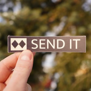 May include: A black and white sticker with a pair of black diamonds and the text "SEND IT" in white letters.