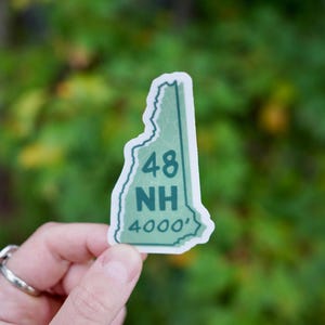 May include: A green and white sticker shaped like the state of New Hampshire with the text "48 NH 4000'" on it.