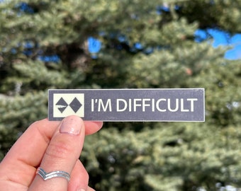 Puede incluir: Una pegatina en blanco y negro con un símbolo de doble diamante y el texto "I'M DIFFICULT".