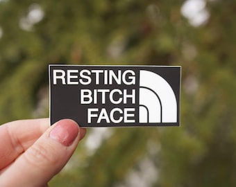 Op de afbeelding: Zwarte en witte sticker met de tekst "RESTING BITCH FACE" en een wit North Face logo.