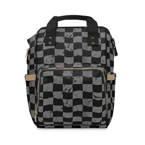 May include: A black and gray checkered backpack with a top handle and adjustable straps. The backpack has a front pocket and side pockets. The zippers are gold-colored. The bag is made of a durable material.