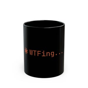 May include: A black ceramic mug with the text "*WTFing..." in a burnt orange colour. The mug is cylindrical and has a glossy finish. The text is in a sans-serif font.