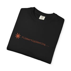 Puede incluir: Camiseta negra con un símbolo de asterisco de color óxido y el texto "Flibbertigibbeting...". La camiseta está hecha de un material suave y tiene cuello redondo.
