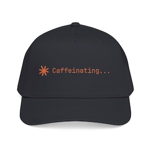 May include: A dark charcoal baseball cap featuring an orange asterisk icon followed by the text "Caffeinating..." printed in a simple sans-serif font on the front center of the crown. The cap has a structured front panel and a curved brim.