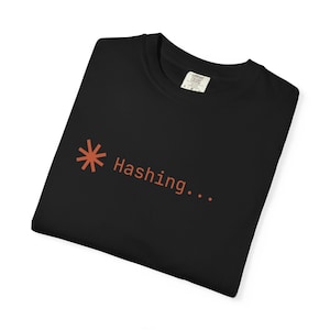 May include: Black t-shirt with the word "Hashing..." in orange, along with an asterisk symbol. The shirt is folded and has a tag on the collar.