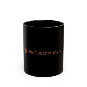 May include: Black ceramic mug with the word "Hallucinating..." in orange text. The mug has a simple, cylindrical shape and a glossy finish. A star-like graphic is next to the word.