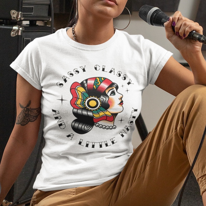 Może przedstawiać: Biała koszulka z nadrukiem kobiety w czerwonym, ż&oacute;łtym i zielonym nakryciu głowy. Wok&oacute;ł grafiki nadrukowany jest tekst "Sassy Classy And A Little Nasty".