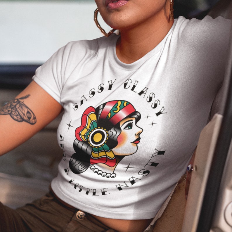 Może przedstawiać: Biała, kr&oacute;tka koszulka z nadrukiem graficznym kobiety w czerwono-zielono-ż&oacute;łtym chustce. Tekst "Sassy Classy And A Little Nasty" otacza grafikę.