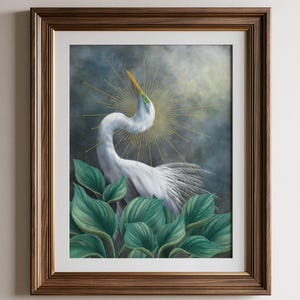 Pode incluir: Uma impress&atilde;o de arte emoldurada apresentando uma gar&ccedil;a branca com pesco&ccedil;o longo e bico amarelo, cercada por grandes folhas verdes. Atr&aacute;s da ave h&aacute; um c&eacute;u escuro e nublado e um design de halo dourado. A moldura &eacute; de madeira castanha.