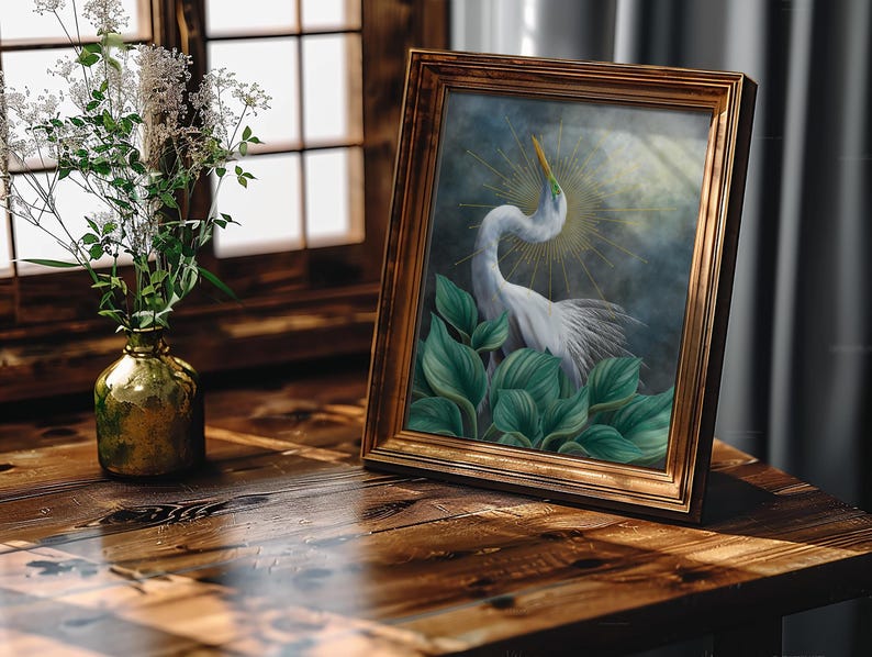 Pode incluir: Uma pintura emoldurada de uma gar&ccedil;a branca com um pesco&ccedil;o longo e curvo, posicionada atr&aacute;s de grandes folhas verdes contra um fundo azul escuro com um halo dourado de raios solares. A obra est&aacute; numa moldura retangular de madeira dourada.