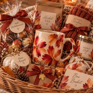 Könnte beinhalten: Ein Geschenkkorb mit einer Keramiktasse mit herbstlichem Blattmotiv, einer Tüte Pralinen mit brauner Schleife, einer Papiertüte mit Aufschrift Herbst TEE, rostfarbenen Strickstrümpfen, einer Kerze mit Aufschrift Herbst Duft, einem Kürbis und Karte.