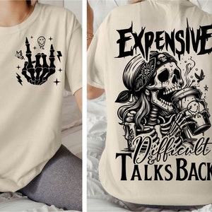 May include: A beige t-shirt with a black skeleton hand making a rock and roll sign on the front and a black skull with a bandana drinking coffee with the text "Expensive & Difficult Talks Back" on the back.