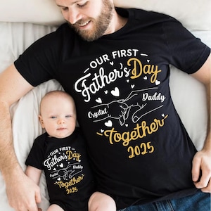 Peut inclure: Un t-shirt noir avec le texte "OUR FIRST Father's Day" en blanc avec des accents dorés. Le texte "Crystal Daddy Together 2025" est également inclus. Un bébé porte un t-shirt assorti.