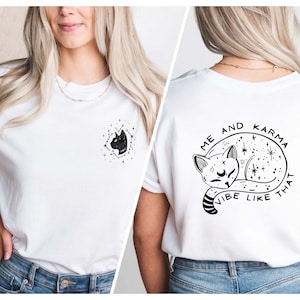 May include: White t-shirt with a black and white graphic of a cat sleeping in a circle of stars. The text "Me and Karma Vibe Like That" is written around the cat.