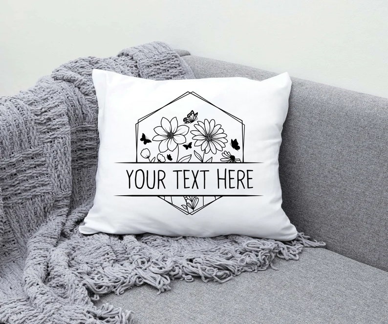 May include: White pillow with a black and white floral design and a geometric frame. The text "YOUR TEXT HERE" is centered below the design.