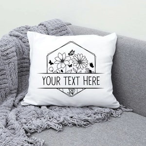 May include: White pillow with a black and white floral design and a geometric frame. The text "YOUR TEXT HERE" is centered below the design.