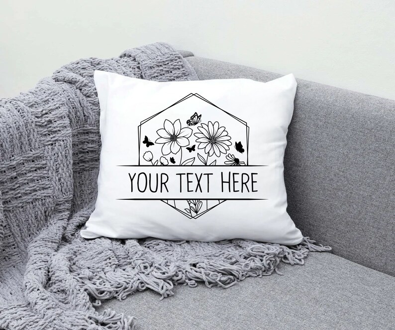 May include: White pillow with a black and white floral design and a geometric frame. The text "YOUR TEXT HERE" is centered below the design.