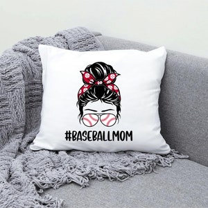 May include: White pillow with a graphic of a woman with a messy bun wearing baseball-themed sunglasses and a red and white headband. The text "#BASEBALLMOM" is printed below the graphic.