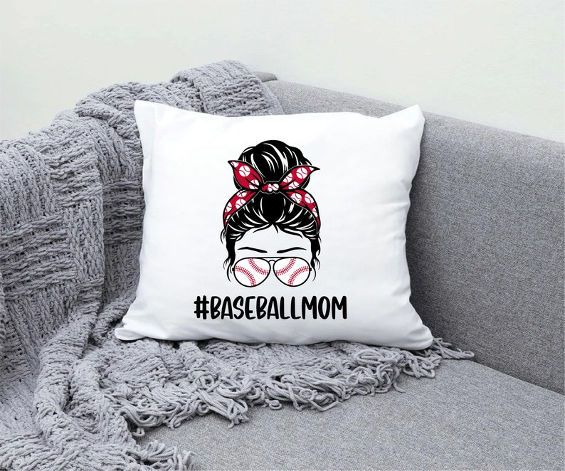 May include: White pillow with a graphic of a woman with a messy bun wearing baseball-themed sunglasses and a red and white headband. The text "#BASEBALLMOM" is printed below the graphic.