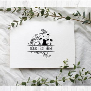 May include: Black and white illustration of a cat sitting in a circle of flowers and butterflies. The text "YOUR TEXT HERE" is written on a banner below the cat.