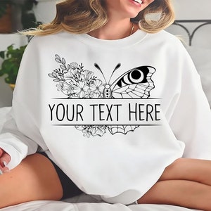 May include: White sweatshirt with a black and white butterfly and floral design. The text "YOUR TEXT HERE" is printed below the butterfly.