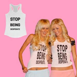 Puede incluir: Dos mujeres con camisetas blancas de tirantes con el texto "STOP BEING DESPERATE" impreso en ellas. Las mujeres sonríen y se miran.