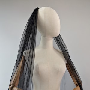May include: A black tulle veil draped over a mannequin with wooden arms. The veil is sheer and delicate, with a soft, flowing texture.