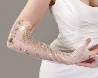 May include: A pair of long white sheer gloves with gold foil accents. The gloves are worn by a person with their arms crossed in front of them.