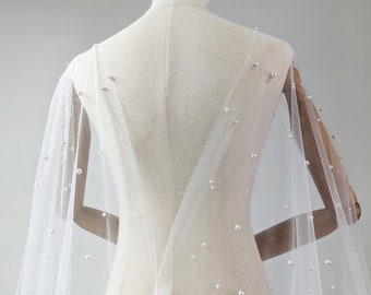 May include: A white tulle bridal veil with scattered pearl embellishments. The veil is draped over a dress form, showcasing the delicate fabric and pearl details.