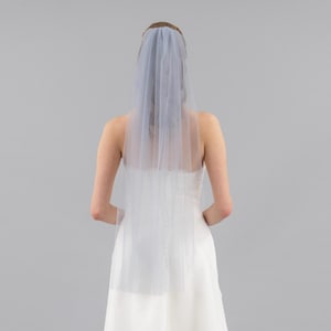 May include: A single-layer tulle bridal veil with a scalloped edge. The veil is worn by a person with their back to the camera.