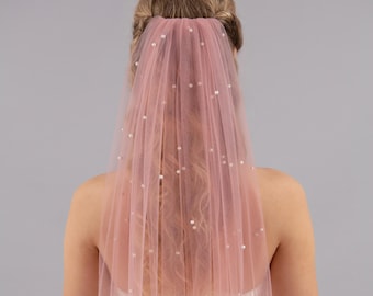 May include: A blush pink bridal veil with pearl embellishments. The veil is made of soft tulle and is perfect for a romantic wedding.