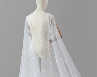 May include: A white tulle bridal cape with pearl embellishments. The cape is draped over a white dress form.