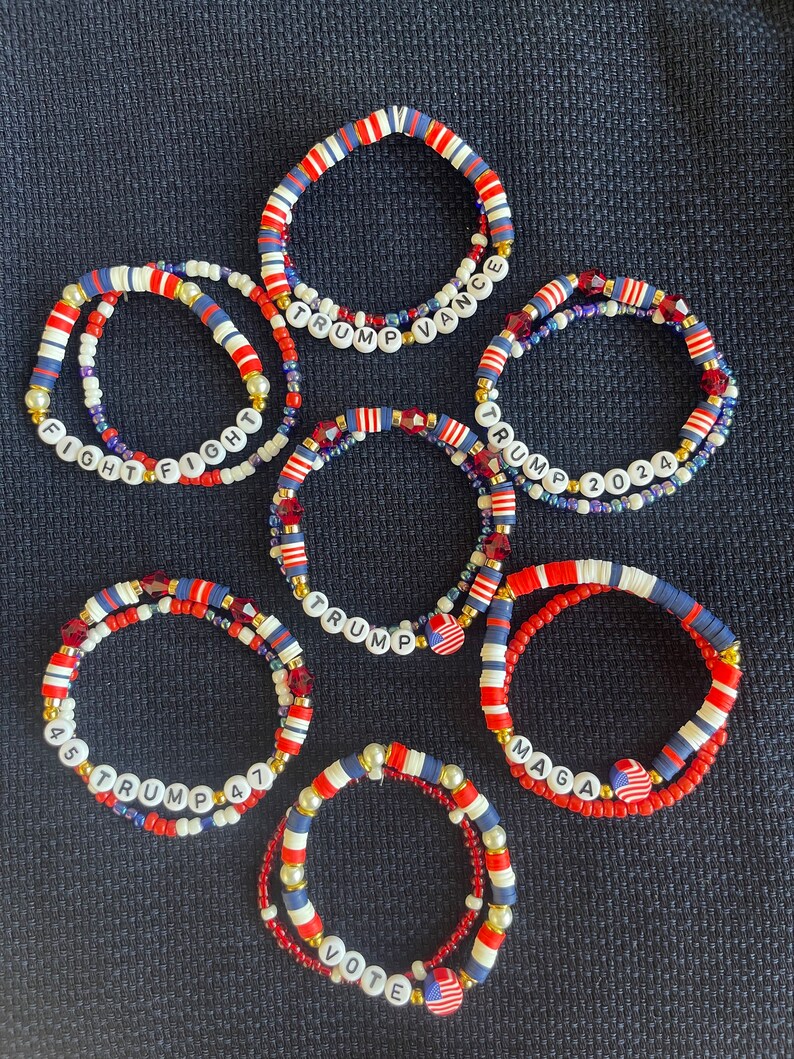 K&ouml;nnte beinhalten: Sechs rot-wei&szlig;-blaue Perlenarmb&auml;nder mit verschiedenen politischen Slogans. Die Armb&auml;nder tragen die Aufschriften "Trump Vance", "Fight Fight", "Trump 2024", "Trump", "45 Trump 47", "Maga" und "Vote".