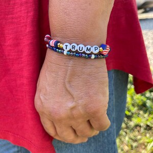 K&ouml;nnte beinhalten: Ein Armband mit roten, wei&szlig;en und blauen Perlen und dem Wort "TRUMP" in wei&szlig;en Perlen.
