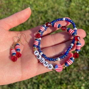 K&ouml;nnte beinhalten: Ein Set aus rot-wei&szlig;-blauen Perlen-Schmuck mit einem Armband, auf dem das Wort "TRUMP" in wei&szlig;en Perlen geschrieben ist und einem amerikanischen Flaggen-Anh&auml;nger. Das Set enth&auml;lt auch ein Paar Ohrringe mit rot-wei&szlig;-blauen Perlen.